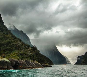 peak of mountain covered with clouds near body of water
