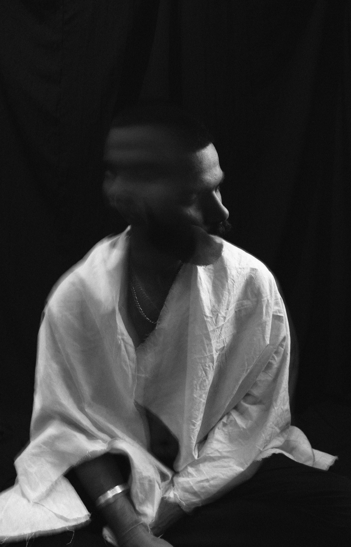 Black and white of lonely melancholic male in white shirt shaking head in motion sitting against black background