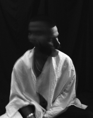 Black and white of lonely melancholic male in white shirt shaking head in motion sitting against black background