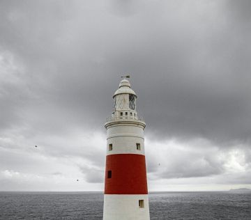 red and white lighthouse under a cloudy sky