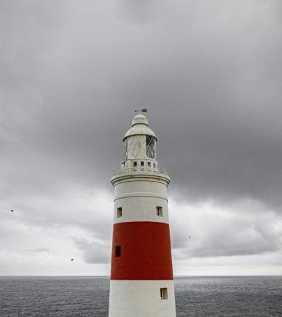 red and white lighthouse under a cloudy sky