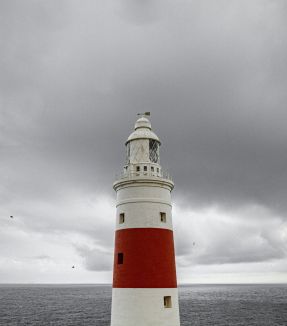 red and white lighthouse under a cloudy sky